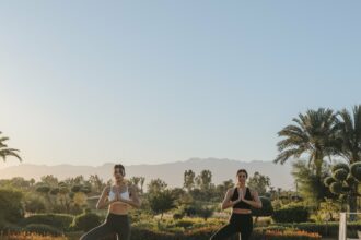 Deux femmes en posture de yoga au lever du jour au Fairmont Royal Palm Marrakech, jardins et Atlas en arrière-plan