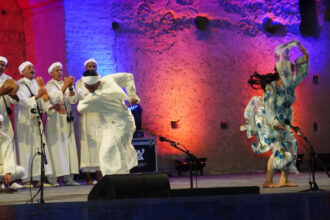 Spectacle nocturne au Festival National des Arts Populaires de Marrakech, troupe en tenue blanche et danseuse au Palais Badiî