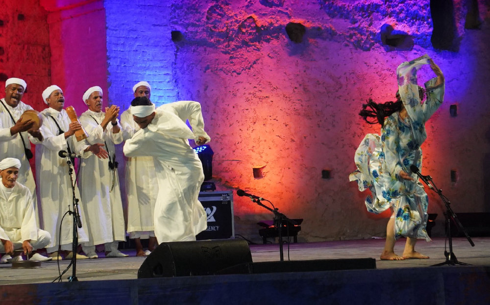Spectacle nocturne au Festival National des Arts Populaires de Marrakech, troupe en tenue blanche et danseuse au Palais Badiî