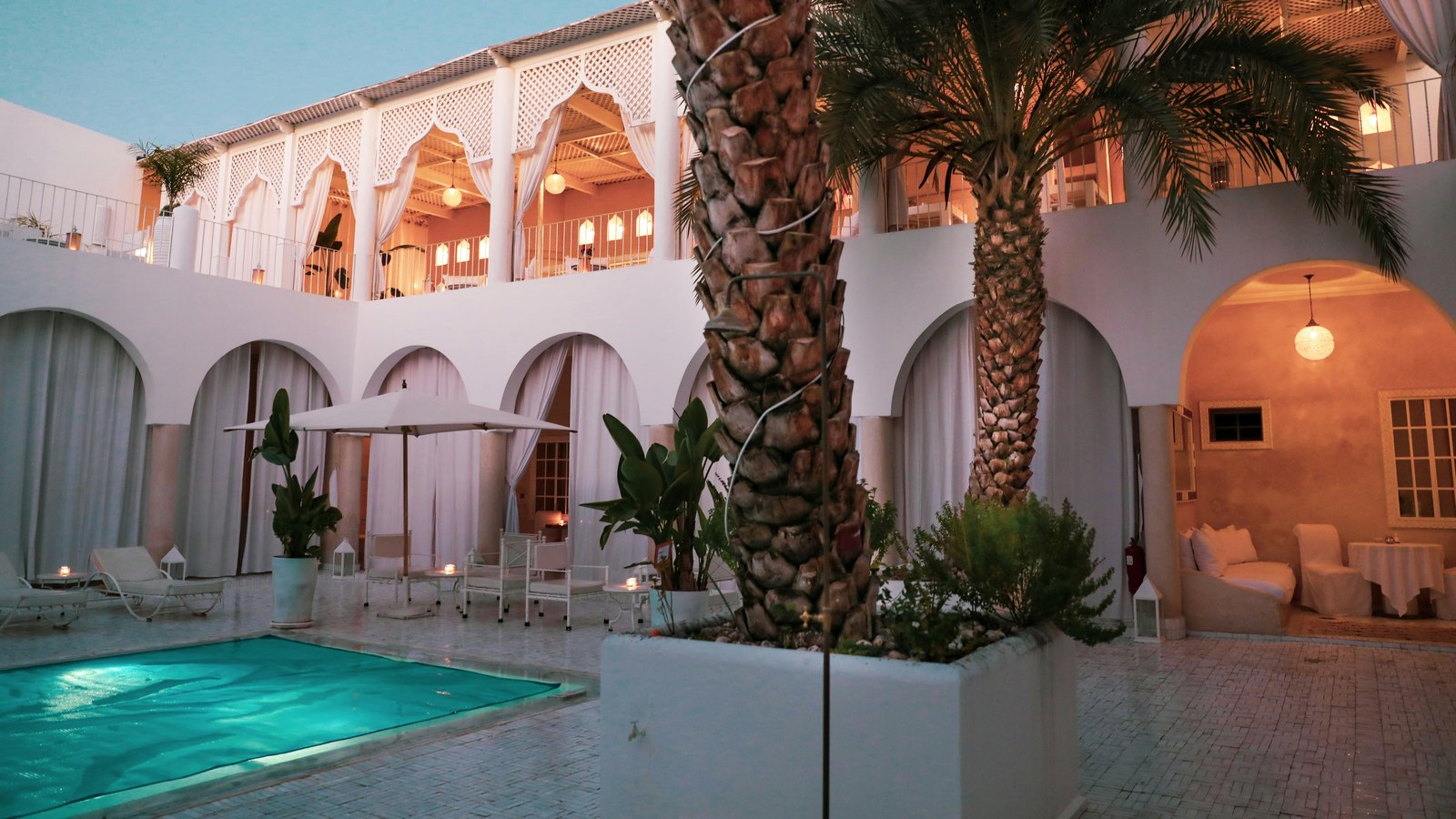 Patio d'un riad à Marrakech au crépuscule, piscine turquoise et palmier — se rafraîchir quand il fait chaud à Marrakech en été.