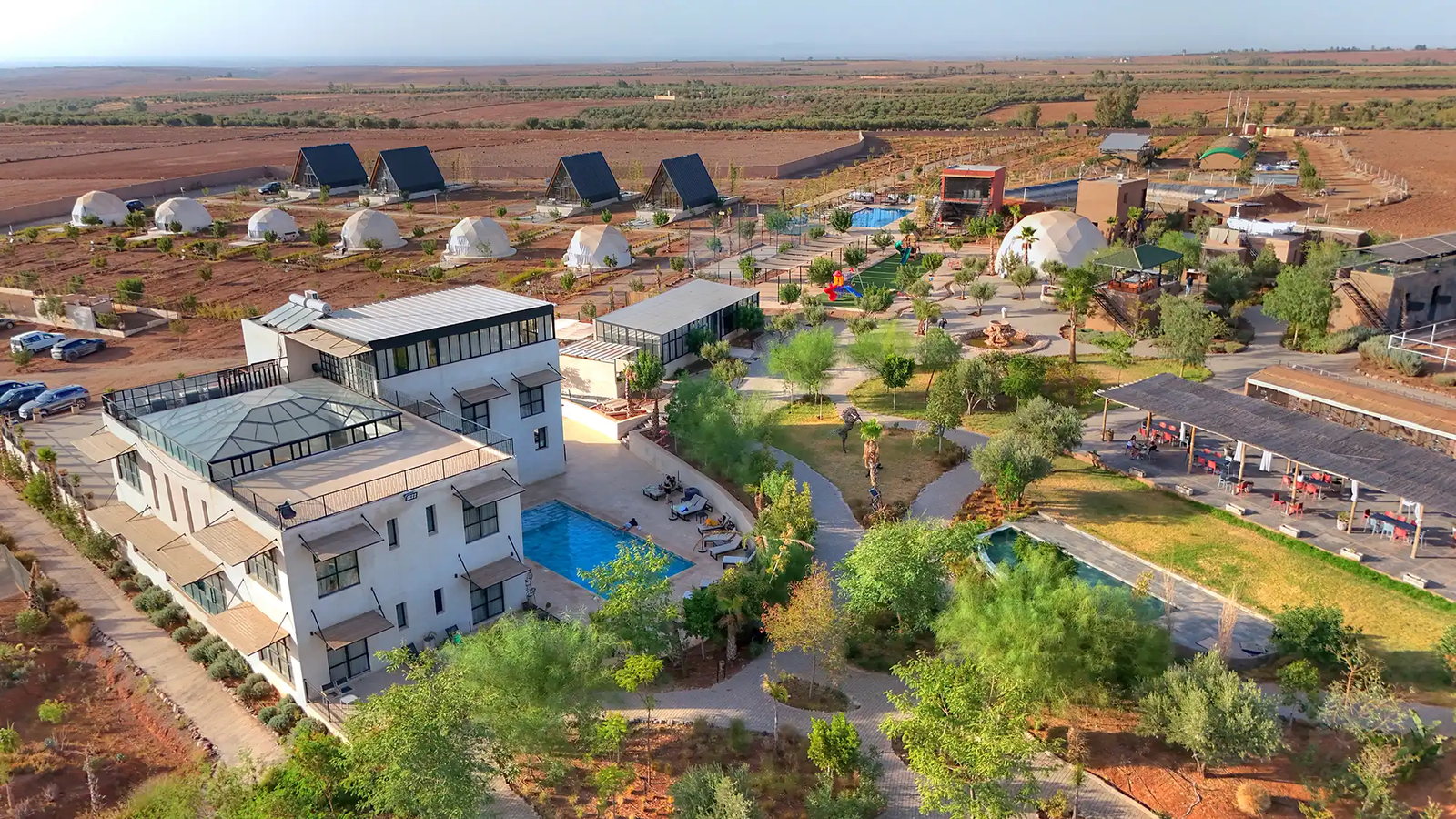 Vue aérienne de The Ranch Marrakech près de Tahannaout : piscine, dômes, aires de jeux et jardins face à la plaine